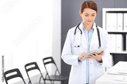 Happy doctor woman at work. Portrait of female physician using tablet computer while standing near reception desk at clinic or emergency hospital. Medicine concept