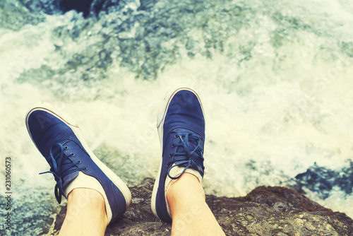 Male legs in blue sneakers against the background of a stream of the mountain river. Traveling concept