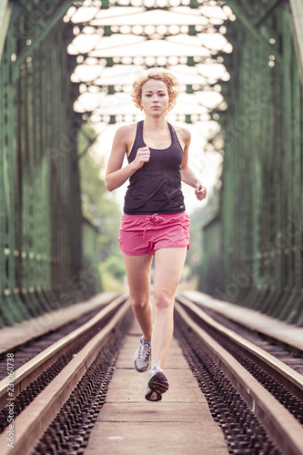 Active sporty woman running on railroad tracks bridge during morning endurance training run. photo