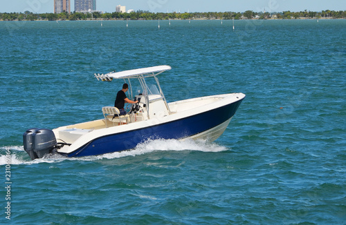 Small open white and blue sport fishing boat powered by two outboard engines.