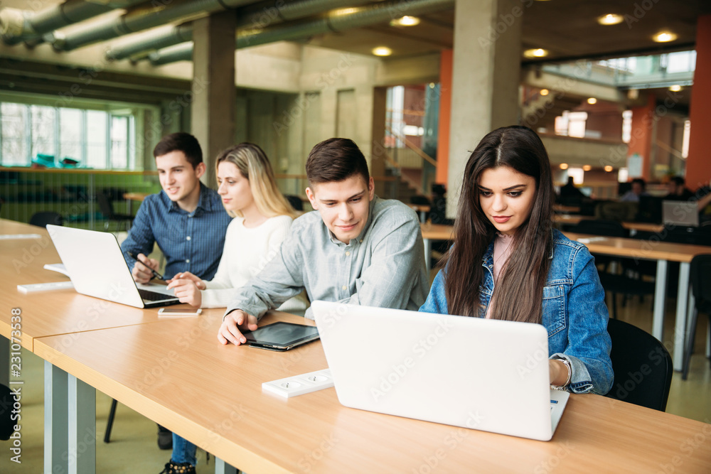 Group of college students studying in the school library, a girl and a boy are using a laptop and connecting to internet Group of college students studying in the school library, a girl and a boy are using a laptop and connecting to internet