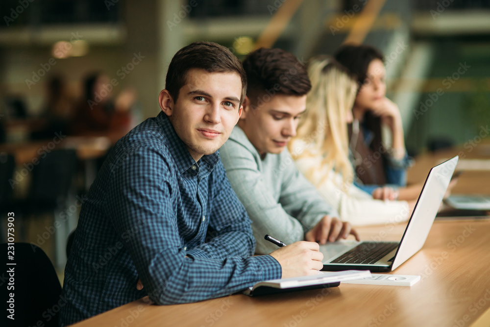 Group of college students studying in the school library, a girl and a boy are using a laptop and connecting to internet. Boy look to the camera Group of college students studying in the school library, a girl and a boy are using a laptop and connecting to internet. Boy look to the camera