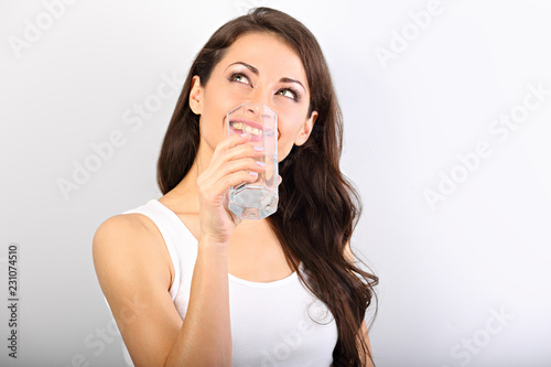 Positive happy smiling woman with healthy skin and long curly hair drinking pure water and looking up on white background. Closeup
