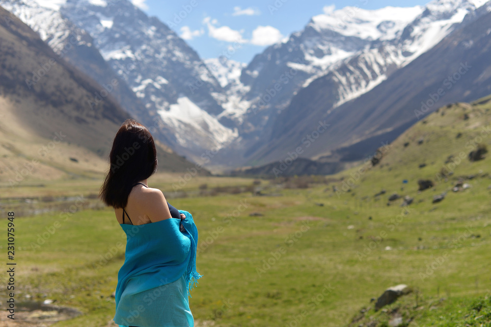 Young woman in t-shirt among snowy mountain peaks.