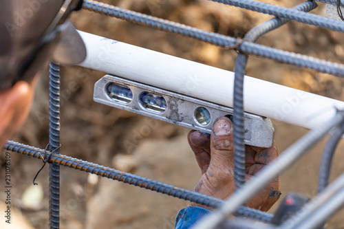 Plumber Using Level While Installing PVC Pipe At Construction Site