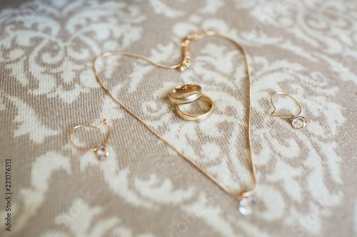 Wedding accessories. Golden necklace, earrings and wedding rings lie on the bed