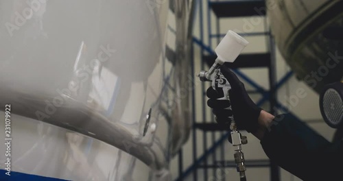 Professional master man in a robe and puller with spray gun puts a layer of paint or ceramics on the yacht. Concept of: Dangerous work, Chemistry, Paints, Garage, Transport Service.