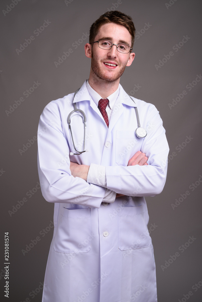 Young handsome man doctor wearing eyeglasses against gray backgr Young handsome man doctor wearing eyeglasses against gray backgr