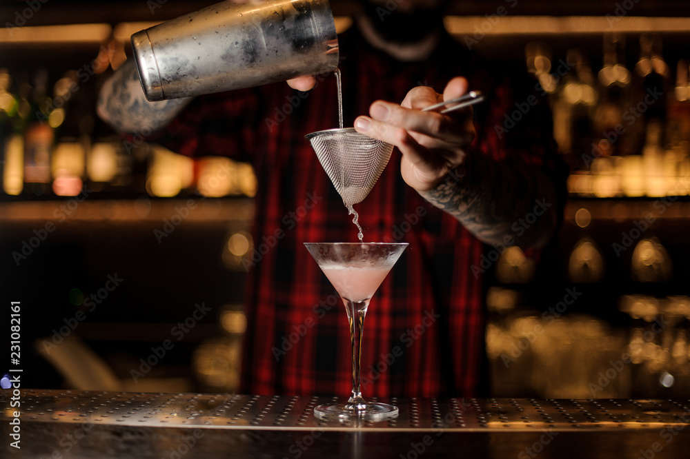Professional bartender pourring a Cosmopolitan from a shaker to a glass