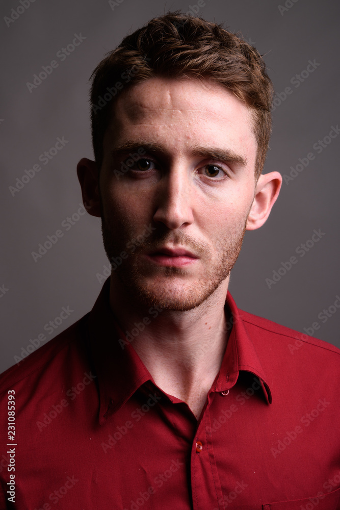 Obraz premium Young handsome businessman wearing red shirt against gray backgr