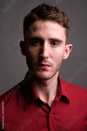 Young handsome businessman wearing red shirt against gray backgr © Ranta Images
