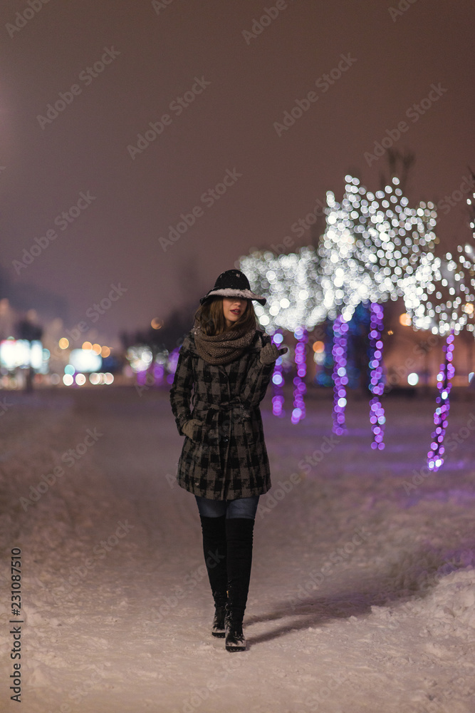 Young girl walking in front of trees decorated with colorful lights for christmas night, blurred in the background