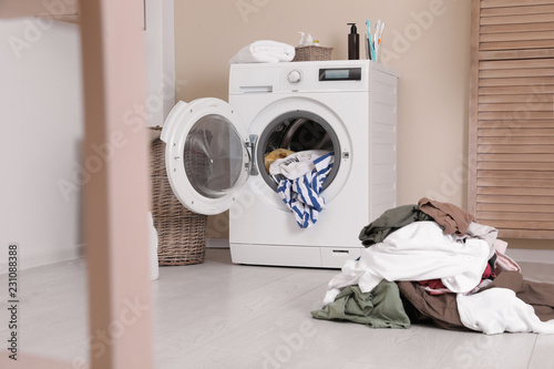Laundry room interior with pile of dirty clothes and washing machine near wall © New Africa