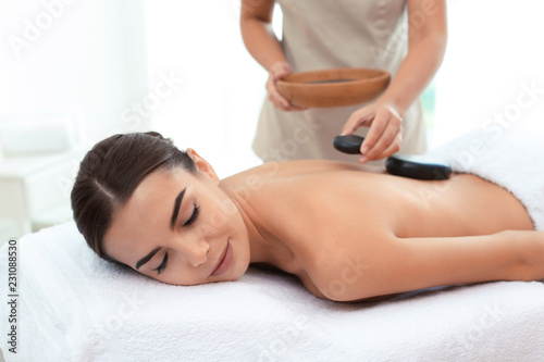 Beautiful young woman getting hot stone massage in spa salon