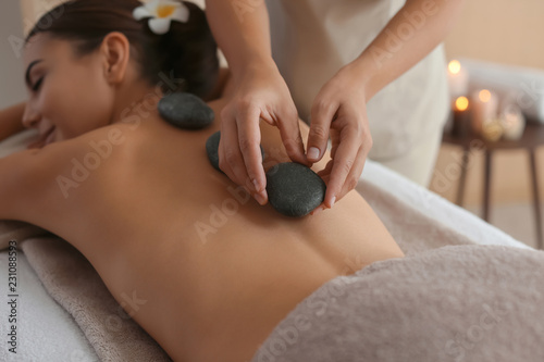 Beautiful young woman getting hot stone massage in spa salon