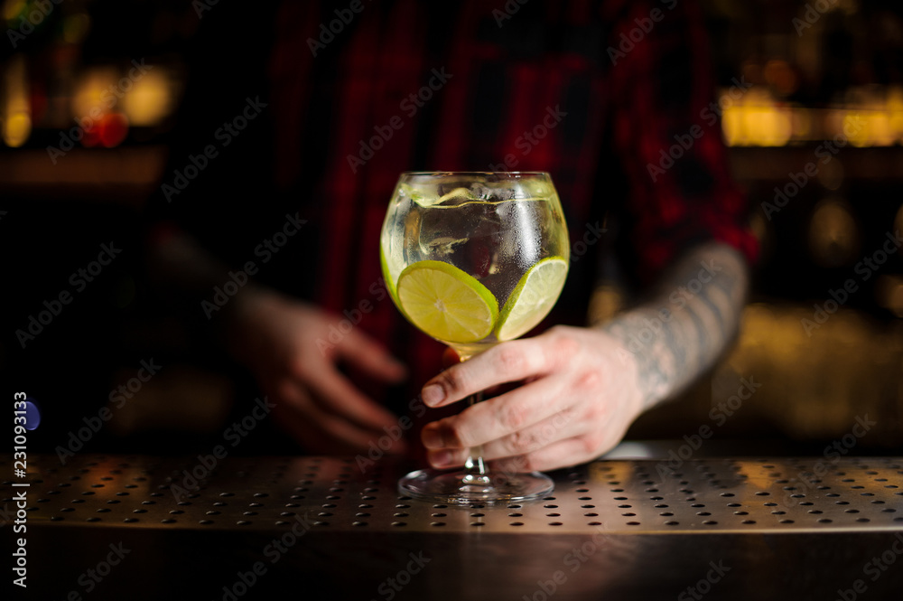 Bartender serving a Gin Tonic cocktail decorated with lime slices