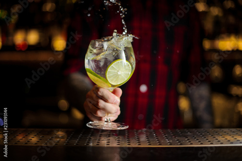 Bartender making splash of a Gin Tonic cocktail decorated with lime slices