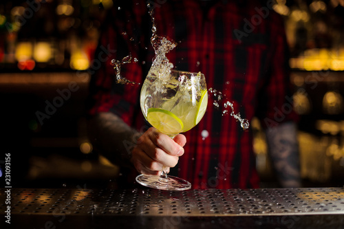 Bartender making splash of a Gin Tonic cocktail with lime slices
