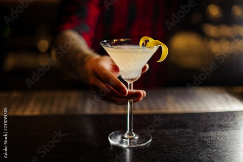 Bartender serving a White Lady cocktail decorated with orange zest