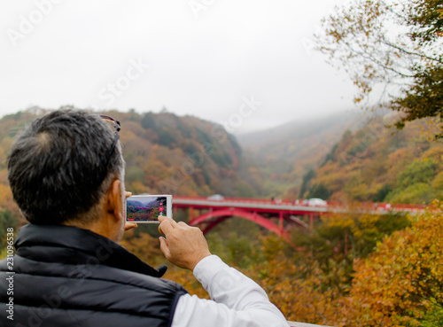 An elderly gentleman taking a video of the Autumn scenery on his smartphone
