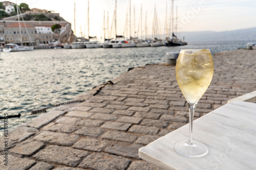 A glass of white wine with ice, at sunset, in the harbor of the enchanting Greek Island of Hydra.