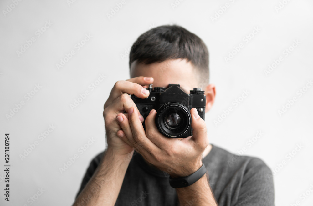 Handsome young bearded man in a black shirt holding vintage old-fashioned film camera on a white background and looking in camera viewfinder. Handsome young bearded man in a black shirt holding vintage old-fashioned film camera on a white background and looking in camera viewfinder.