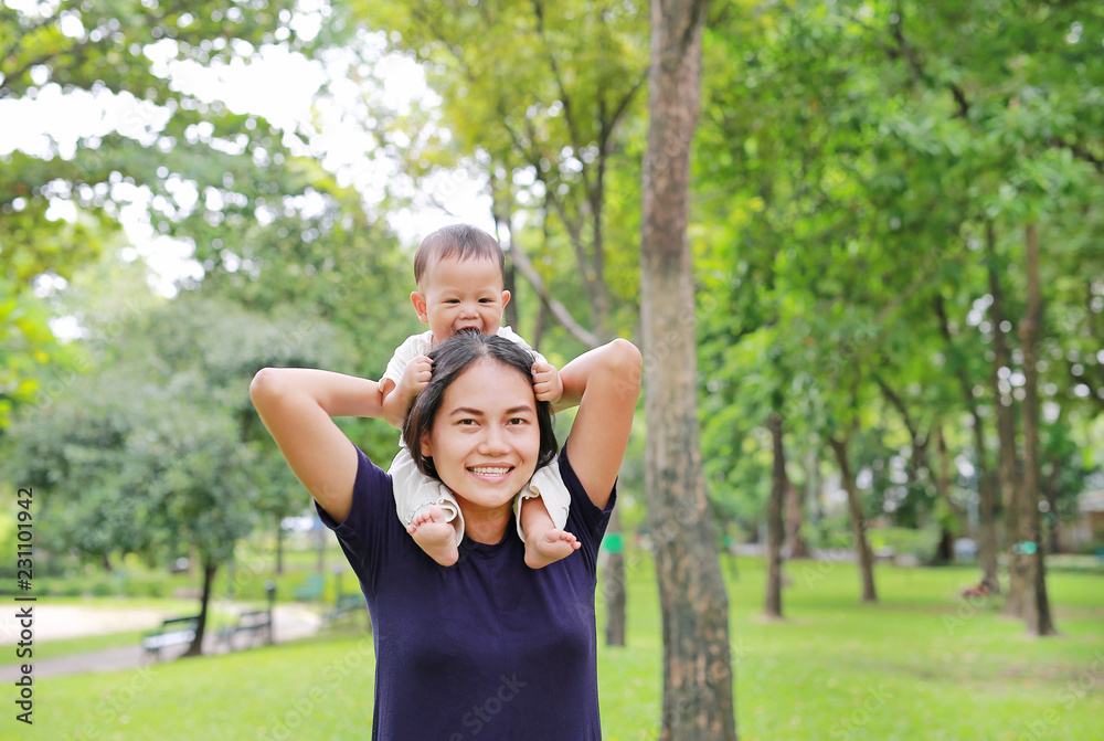 Obraz premium Beautiful young Asian mother with happy baby boy riding on mom's shoulder in the nature park.