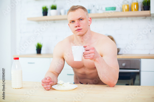 Muscular man with a naked torso in the kitchen with milk and cottage cheese, the concept of a healthy diet. Athletic way of life.