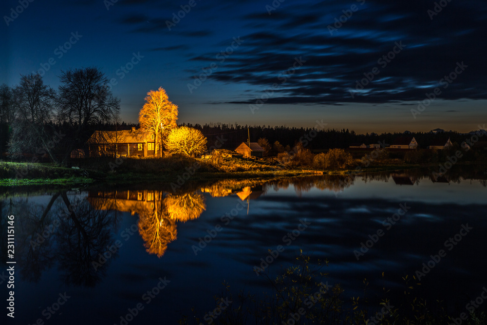 Night by the river. Black River. Reflection of houses in the water. River bank and reflections in the water. Trees are reflected in the water. The village on the banks of the river. Night light lanter