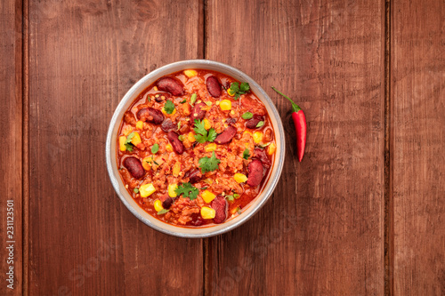 A photo of chili con carne with a chilli pepper, shot from above on a dark rustic wooden background with copy space