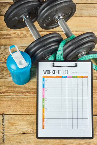 Healthy lifestyle concept. Mock up on workout and fitness dieting diary. Workout log sheet, blue shaker, measuring tape and dumbbells on a wooden background