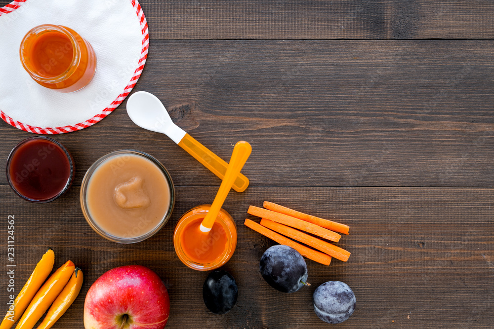 Ingredients for baby puree. Assortment of flavors of baby food. Vegetables and fruits. Apple, carrot, pumpkin, prune near bib on dark wooden background top view space for text Ingredients for baby puree. Assortment of flavors of baby food. Vegetables and fruits. Apple, carrot, pumpkin, prune near bib on dark wooden background top view space for text