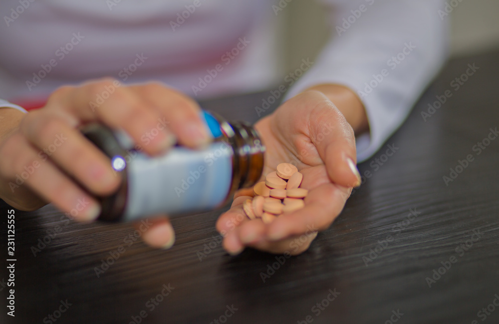 Woman hands holding bottle of pills in one hand and pile of tablets on other hand.