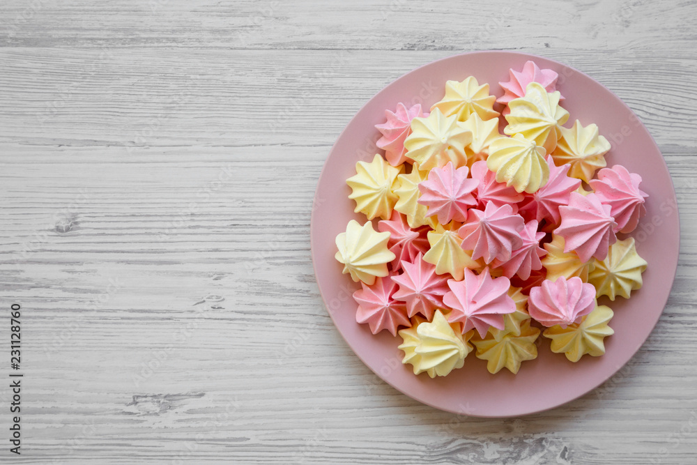 Mini meringues on pink plate on a white wooden background, top view. Close-up. Copy space. Mini meringues on pink plate on a white wooden background, top view. Close-up. Copy space.