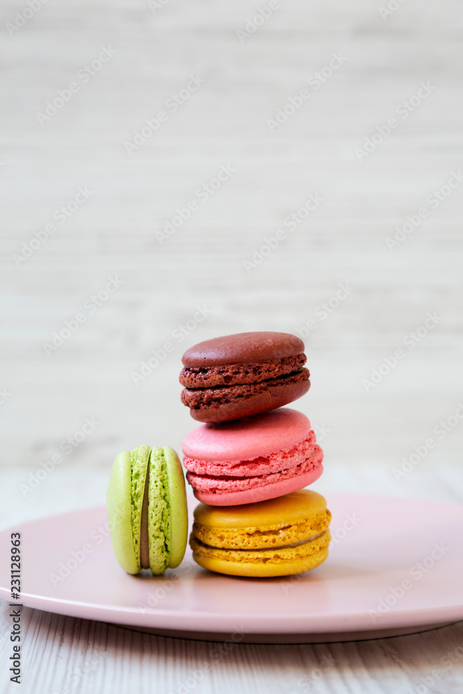 Sweet and colorful macaroons on pink plate on a white wooden background, side view. Close-up. Sweet and colorful macaroons on pink plate on a white wooden background, side view. Close-up.
