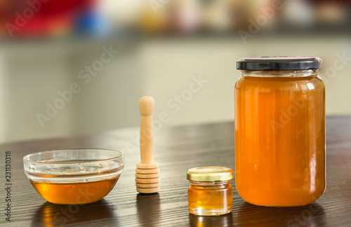 Small and big jar of honey with small bowl on kitchen background.