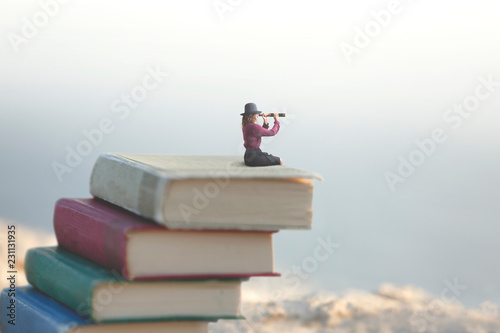 miniature woman looks at the infinity with the spyglass on a scale of books