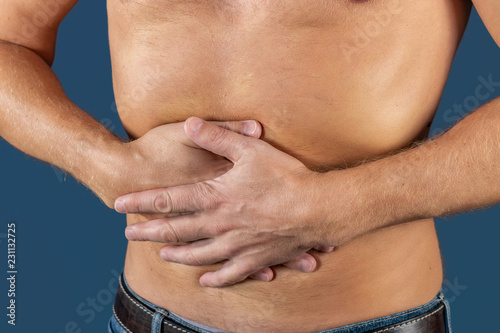 Man holding his stomach in pain. Man with naked torso experience stomachaches on blue background. Medical concept