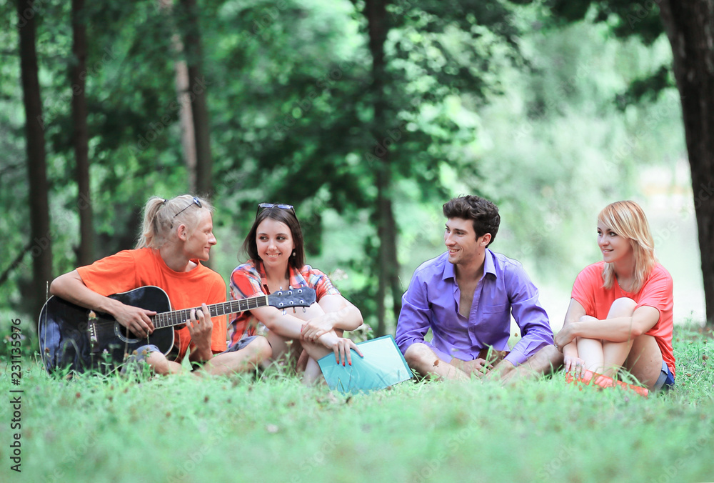 group of students sing songs sitting on the lawn in the city Park group of students sing songs sitting on the lawn in the city Park