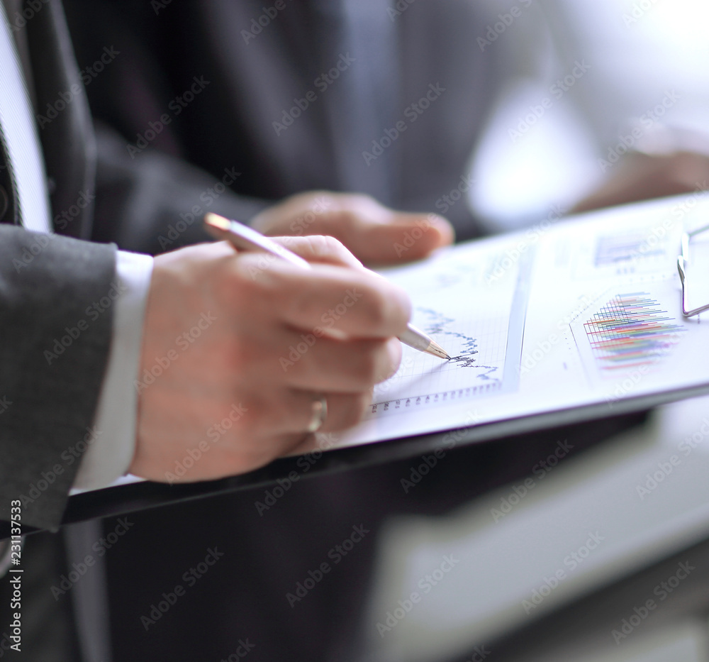 businessman at desk checking a financial report and pointing at a bar chart with a pen businessman at desk checking a financial report and pointing at a bar chart with a pen