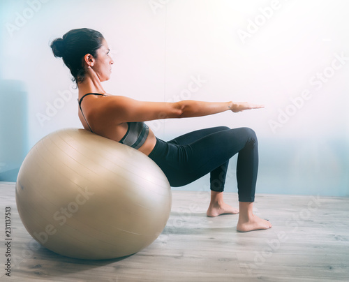 Woman working out with exercise ball in gym. Pilates woman doing exercises in the gym workout room with fitness ball. Fitness woman doing exercises for muscle press with abs swiss ball. photo