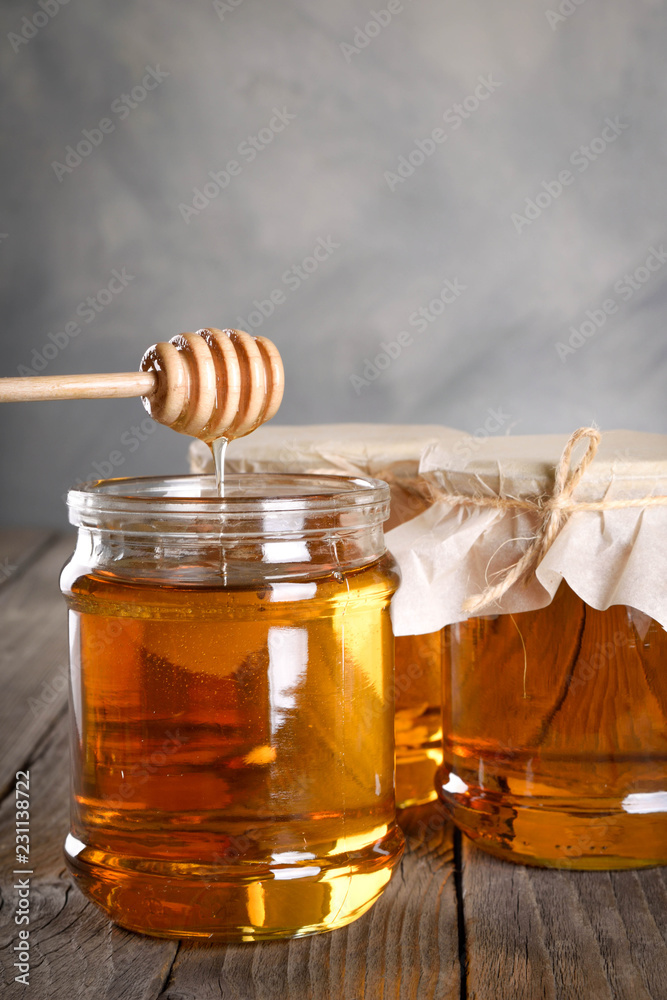 Pouring aromatic honey into jar, closeup. Honey in glass jars and honeycombs wax on wooden background. Wooden stick , instruments Pouring aromatic honey into jar, closeup. Honey in glass jars and honeycombs wax on wooden background. Wooden stick , instruments