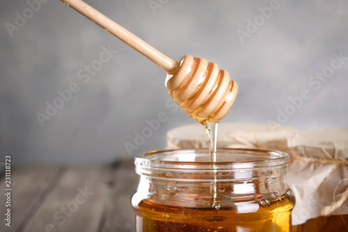 Pouring aromatic honey into jar, closeup. Honey in glass jars and honeycombs wax on wooden background. Wooden stick , instruments