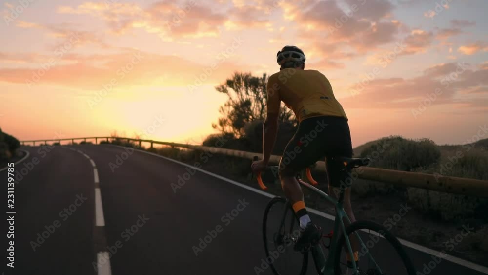 A young sports man riding a bike on a mountain serpentine in a yellow t-shirt helmet and sports equipment rear view . Slow motion steadicam