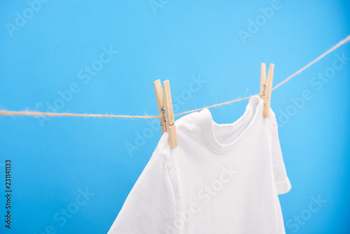 clean white t-shirt with clothespins hanging on rope isolated on blue