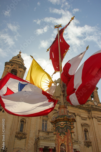 Waving red, yellow and white flags on festively decorated square near old church for annual festa religious holiday