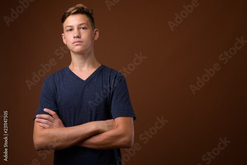 Studio shot of young handsome teenage boy against brown backgrou