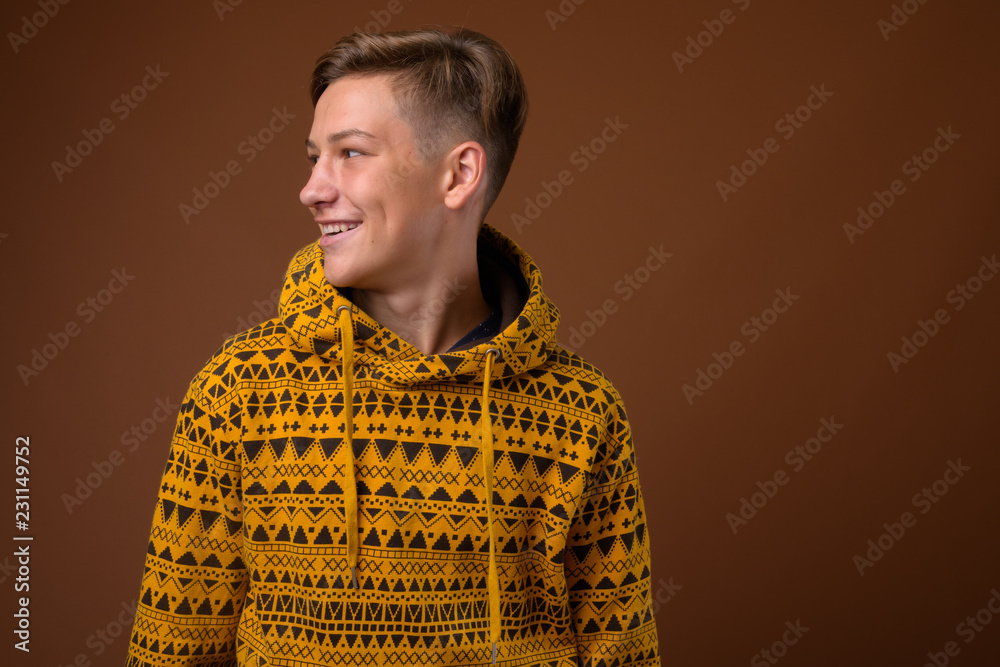 Fototapeta premium Studio shot of young handsome teenage boy against brown backgrou