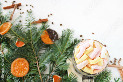 holidays, winter and celebration concept - hot chocolate drink with marshmallows, cinnamon, dry oranges, coffee beans and fir tree on white background. Winter christmas holiday background. Flat lay