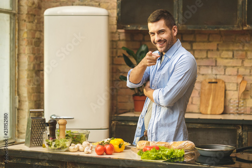 Portrait of young man preparing delicious and healthy food in the home kitchen on a sunny day. Smiling and looking at camera.
